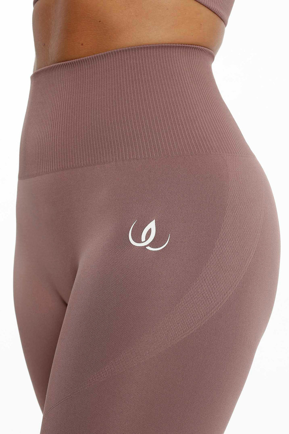 Den ribbede linningen og den hvite logoen på hoften, stoffet i en dempet rosabrun tone.