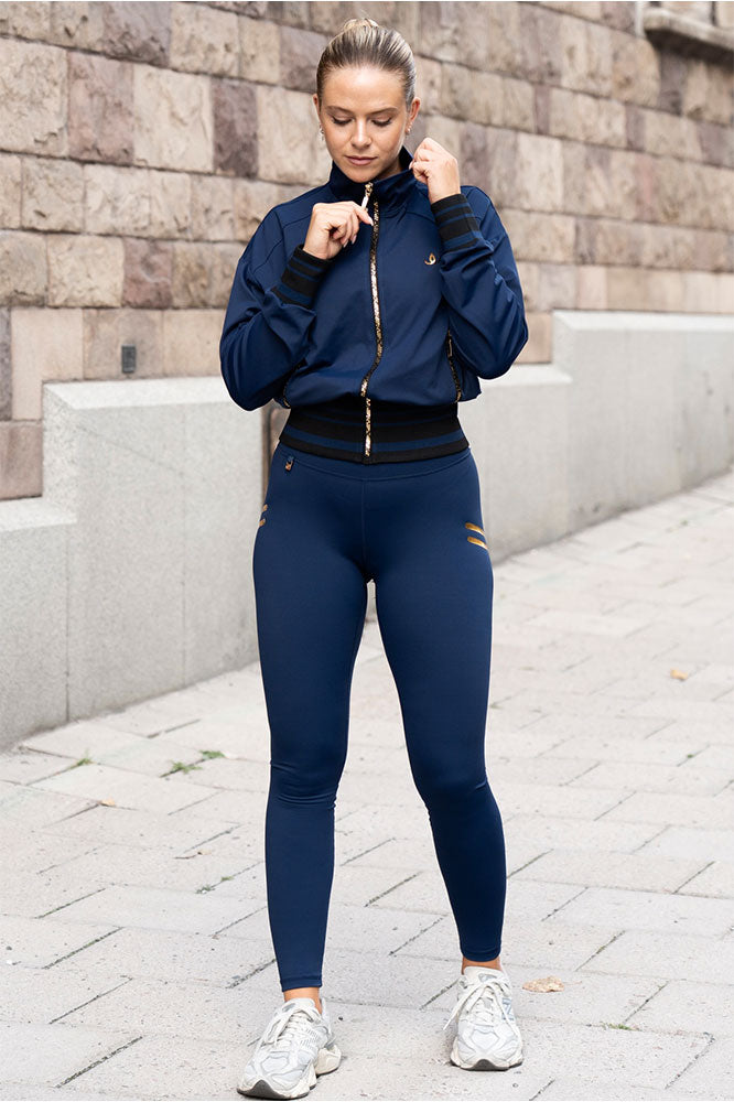 På fortauet bæres den marineblå jakken åpen i halsen, til tights med gullstriper og hvite sko.