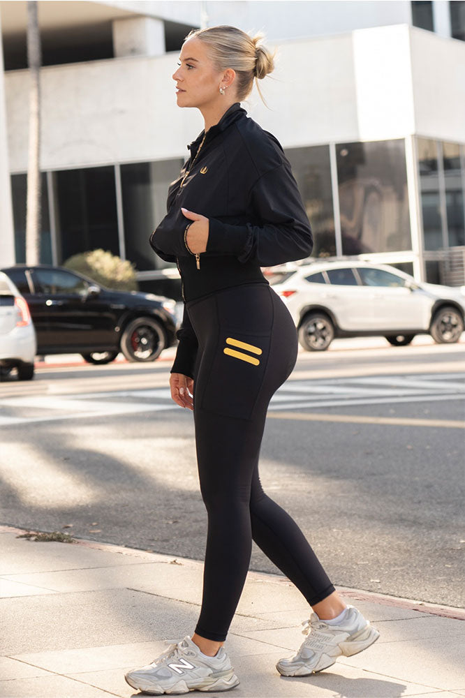 Modellen går langs gaten i svarte tights med gullstrek på lommen og svart jakke.