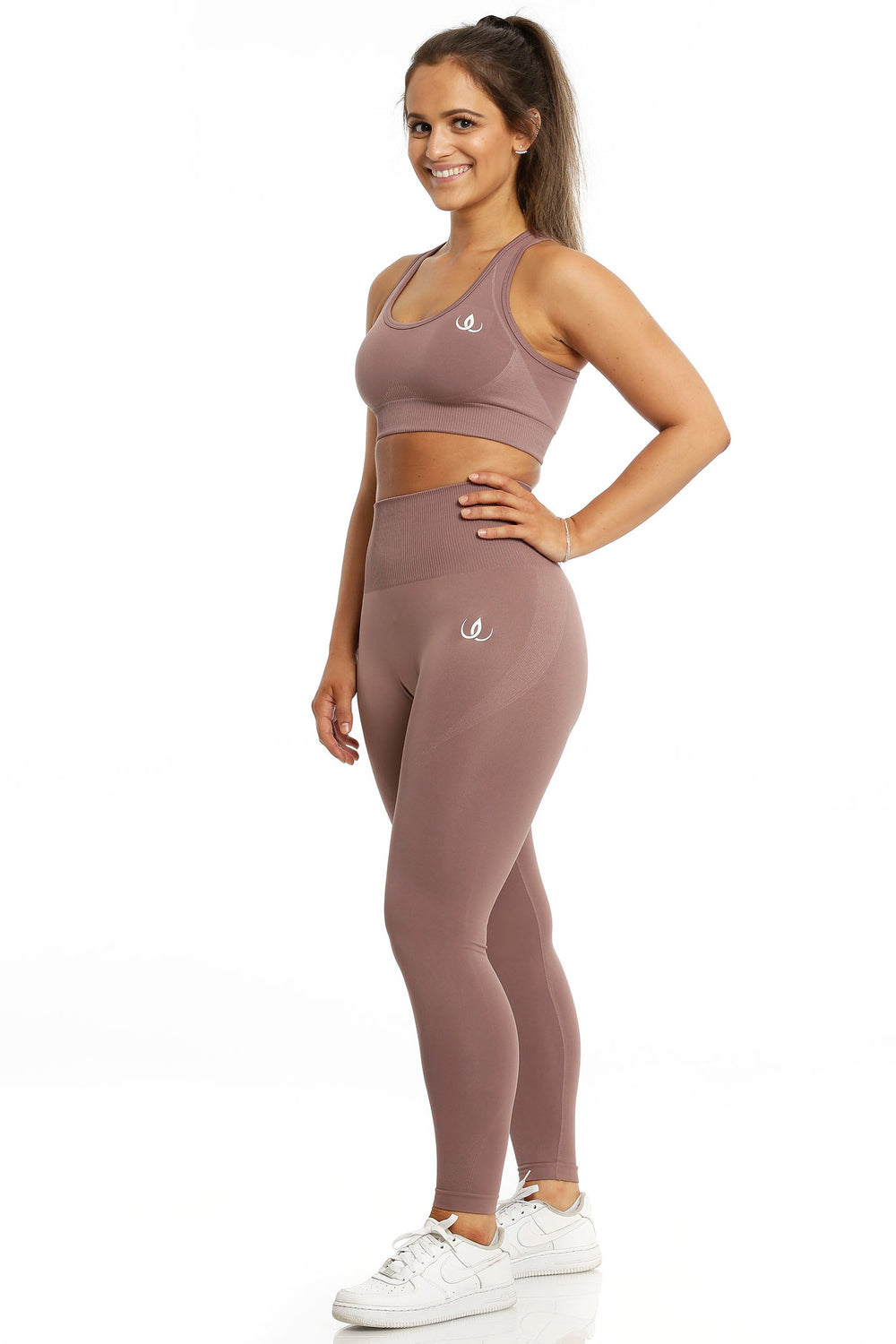 Sports-bh og tights i samme rosabrune tone. Modellen står med hånden i siden, i hvite sko.