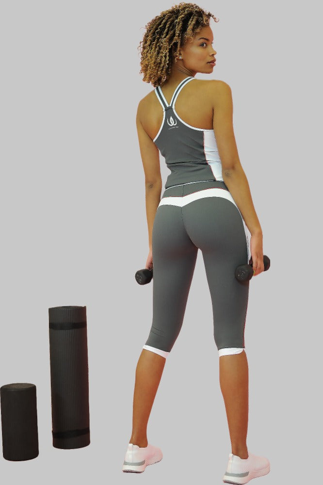 Grå capritights med hvite kanter ved knærne, båret til grå singlet. Modellen holder to håndvekter.