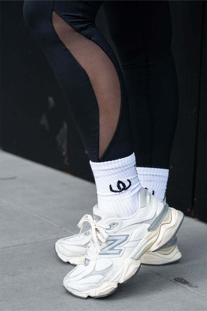 Hvite sokker med svart logo båret til hvite sneakers og svarte tights med meshinnsats.