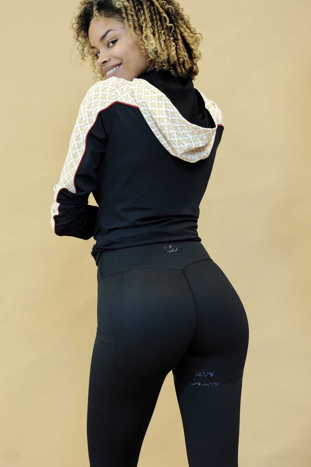 Over skulderen synes jakkens gullmønstrede hette og røde kantlinje. Modellen bærer svarte tights.