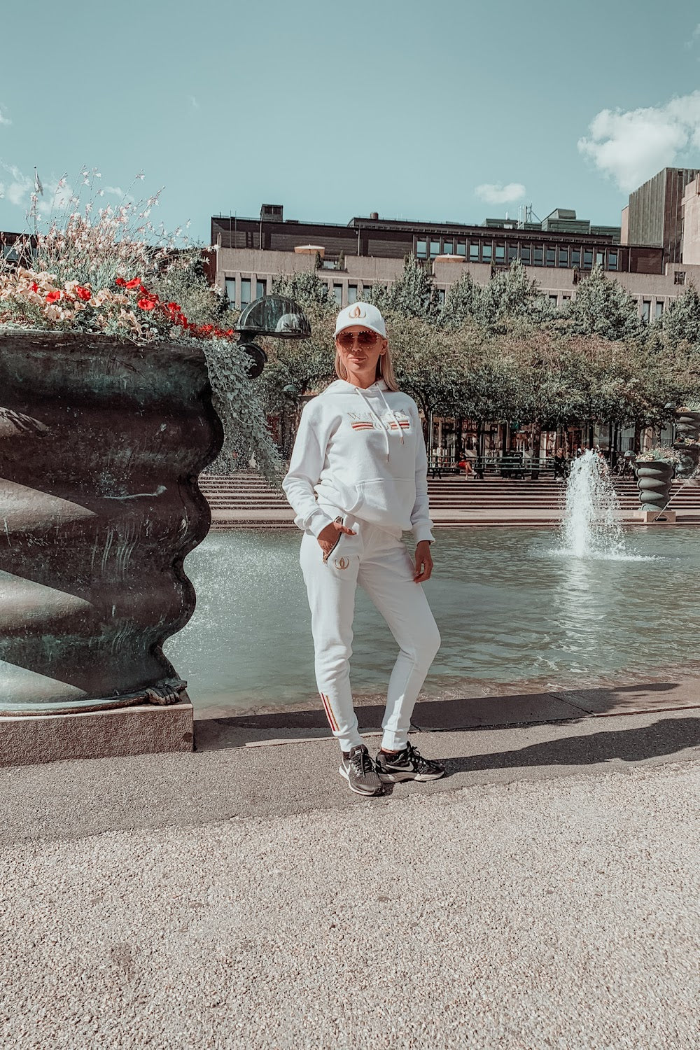 Foran fontenen står modellen i hvit hettegenser, hvite joggers og hvit caps.