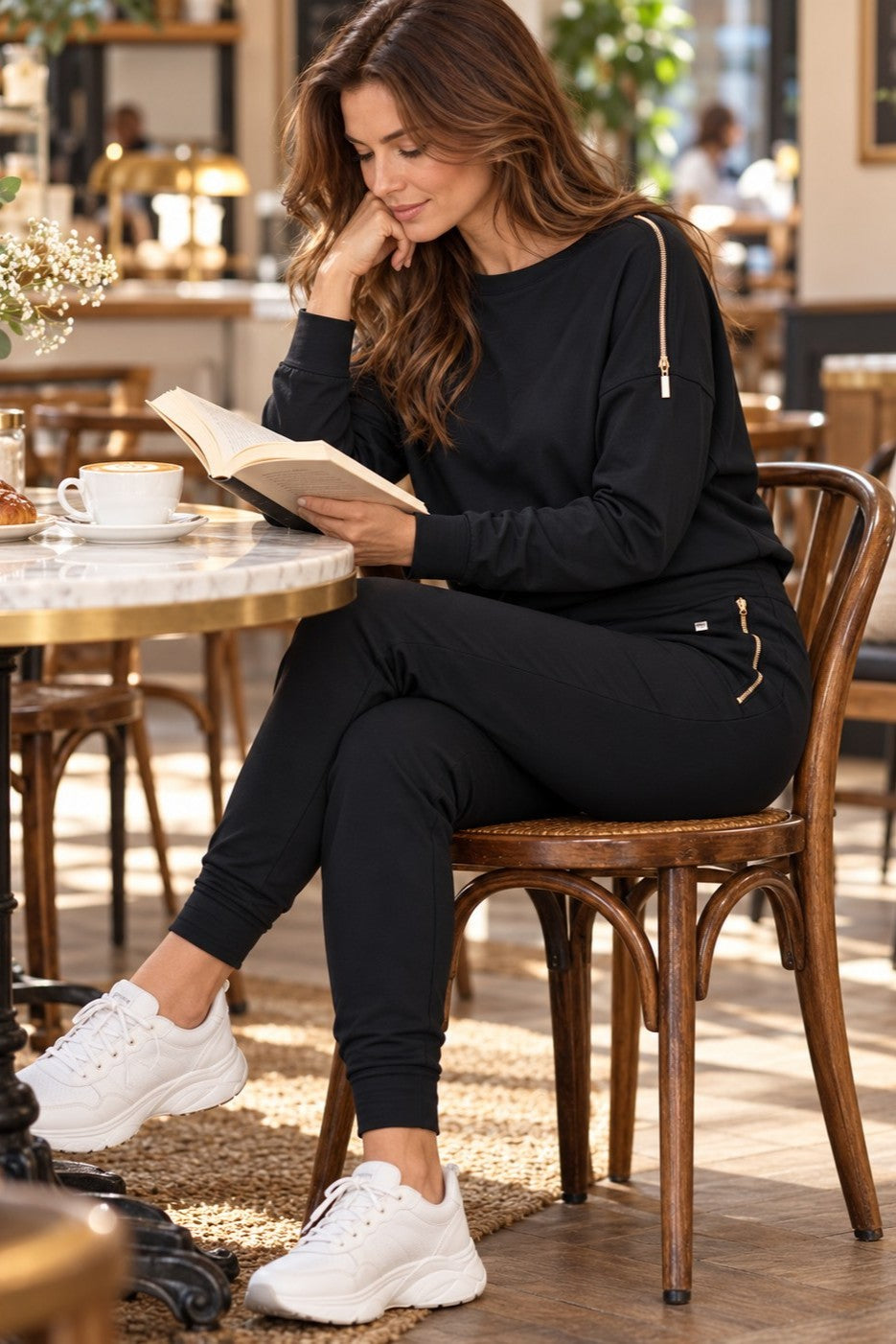 Edge Casual Zip-settet i svart på en kafé, med en bok og en kopp kaffe.